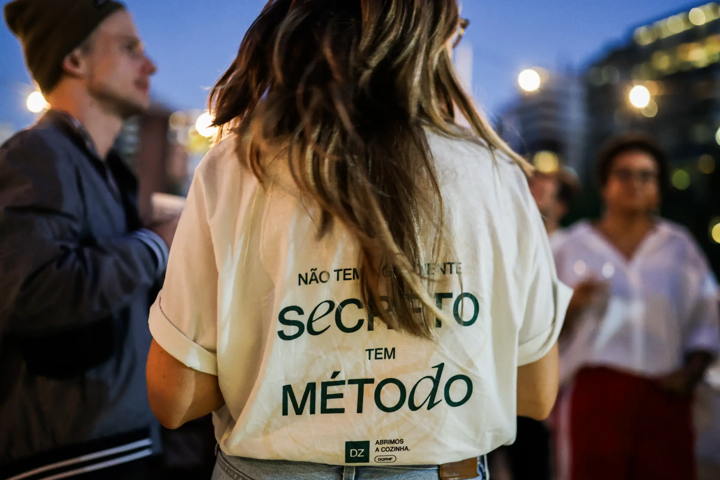 Pessoa de costas no DZ Day 2026, com a camiseta “Não tem segredo, tem método”
